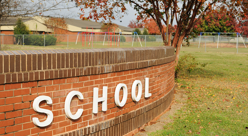Short brick wall with a sign reading 'school' across it, sits in front of a building.