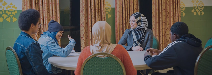 Roula Allouch sits at a table talking with young adults.