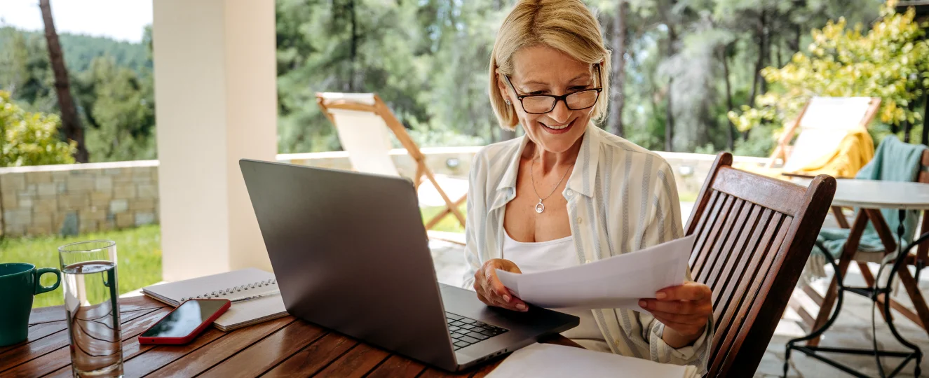 Smiling woman working on laptop at back yard of her house